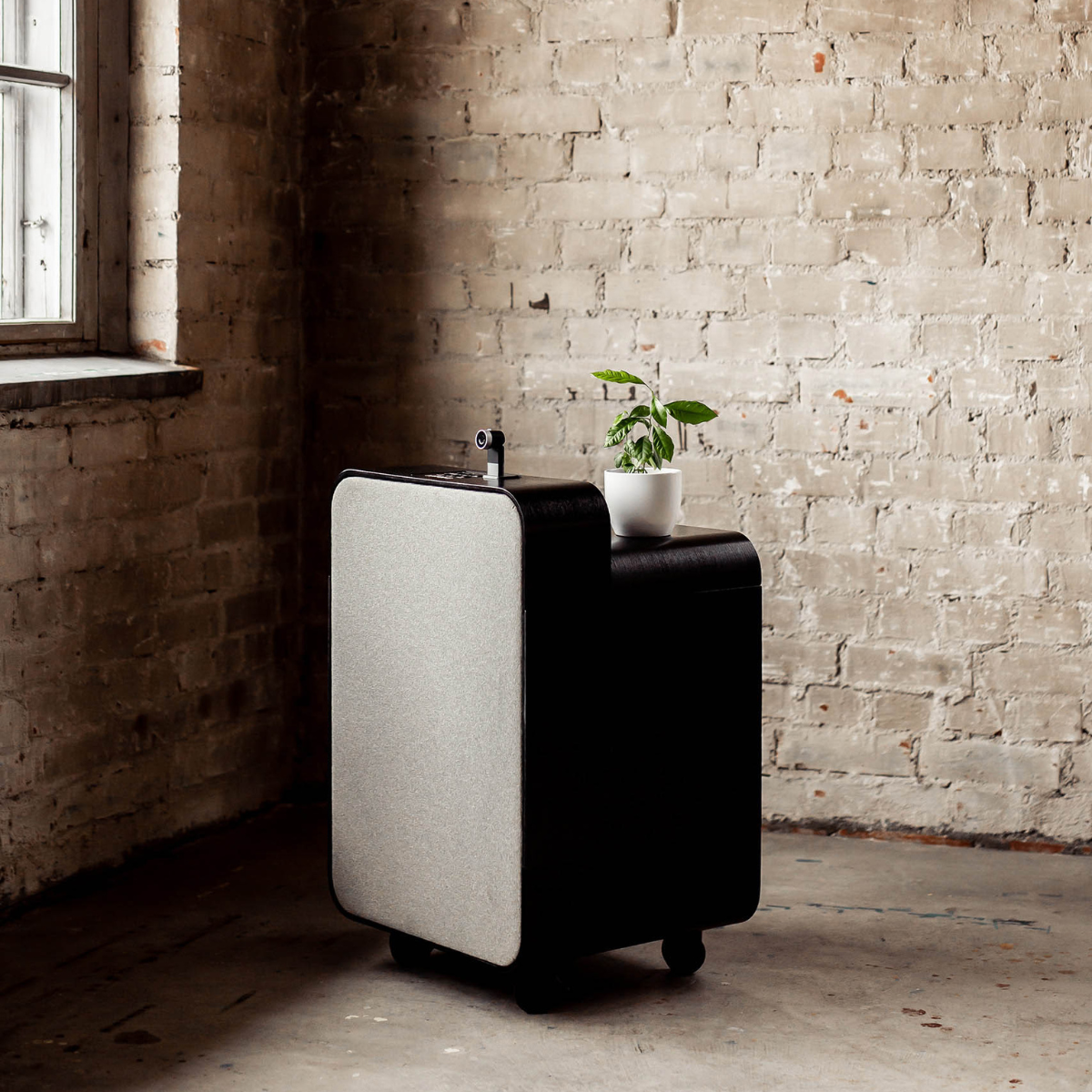 Artome M10 in black with a light grey front, standing against a brick wall